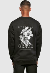 Black sweatshirt featuring a large white floral design on the back with the text "ETERNAL GRACE" above and below the graphic.