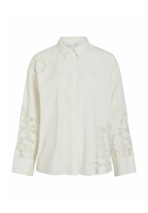 Vit skjorta med knäppning framtill, utrustad med långa ärmar och blommönstrad broderi på axlarna och ärmarna, tillverkad av lätt tyg.