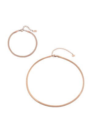 Nahaufnahme einer Person, die eine dünne, glatte Halskette aus Roségold und ein weißes, geripptes Tanktop trägt.