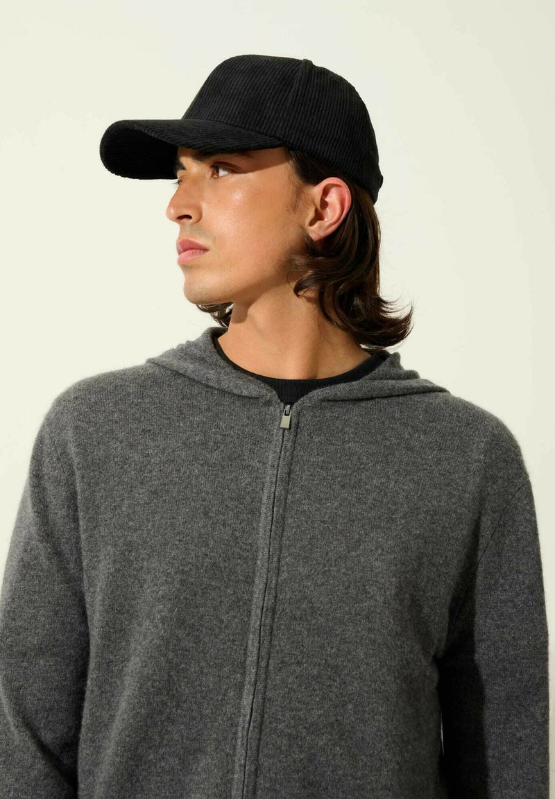 Szara bluza z kapturem na zamek, o miękkiej fakturze, zestawiona z czapką z grubego materiału w kolorze czarnym, z wygiętym daszkiem.