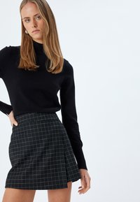 Maglione nero con scollo alto abbinato a una mini gonna a quadretti bianca e nera. La gonna presenta un design plissettato e tasche laterali.