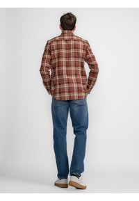 Camisa de cuadros en marrón y crema, con mangas largas y cuello puntiagudo. Combinada con jeans azules y zapatillas blancas.