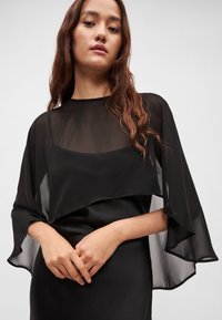 Černé šaty s průsvitnou vrstvou a širokými rukávy, hladkou texturou a přiléhavým střihem, zdůrazňující vrstvený design.