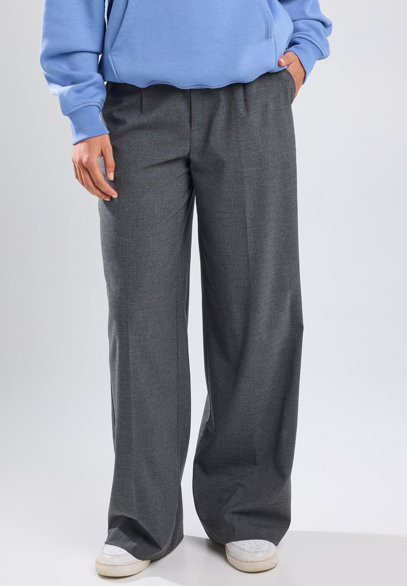 Gray wide-leg trousers made from textured fabric, featuring a high waist and pleated front, paired with a blue sweatshirt and white sneakers.