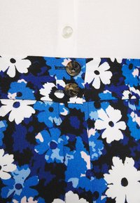 Falda floral con flores azules y blancas sobre un fondo negro, con dos botones marrones en la cintura y una tela suave y texturizada.