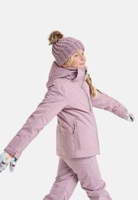 Fialová lyžiarska bunda s kapucňou a zipsom, kombinovaná s pásikmi. Svetrová pletená čiapka s pom-pomom. Farebné vzorované rukavice.