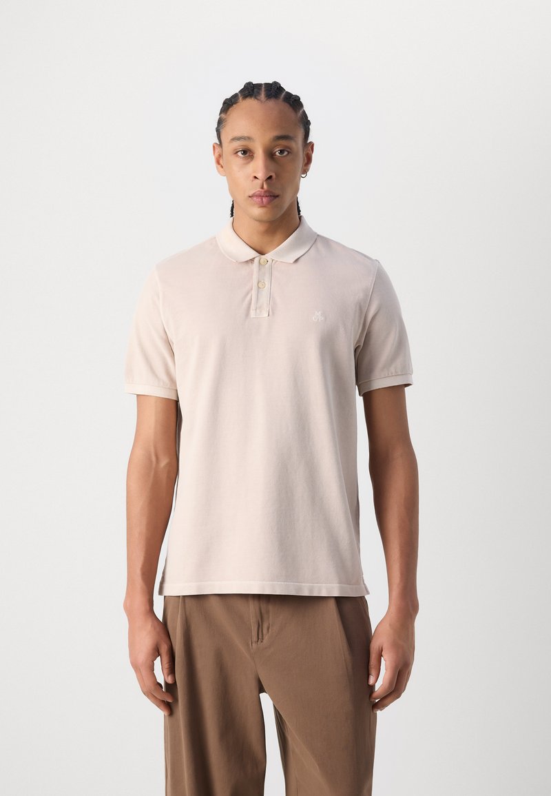 Jasno beżowa koszulka polo wykonana z bawełny, z kołnierzykiem, dwoma guzikami, krótkimi rękawami oraz wyszywanym logo na klatce piersiowej.