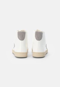 Botas de tornozelo brancas com um cabedal de couro liso, detalhes em camurça cinza no calcanhar e uma sola de borracha bege. Apresenta elementos de design minimalistas.