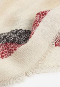 Tissu doux tissé avec des bords effilochés, présentant des blocs texturés de couleurs crème, rouge et gris foncé.