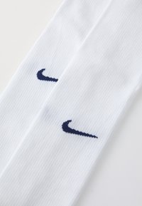 Białe skarpetki sportowe Nike z fakturą prążkowaną. Zawierają niebieską logo Swoosh na każdej skarpetce dla oznaczenia marki.