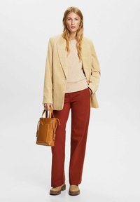 Blazer de pana beige, suéter ligero, pantalones color óxido, zapatos de plataforma marrones y una pequeña bolsa de mano de tan con detalle de bolsillo.