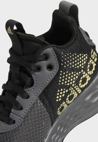 Scarpa da atletica nera con tomaia in mesh e materiale sintetico, caratterizzata da accenti grigi e dettaglio del logo giallo sul lato. Suola in gomma con motivo testurizzato.