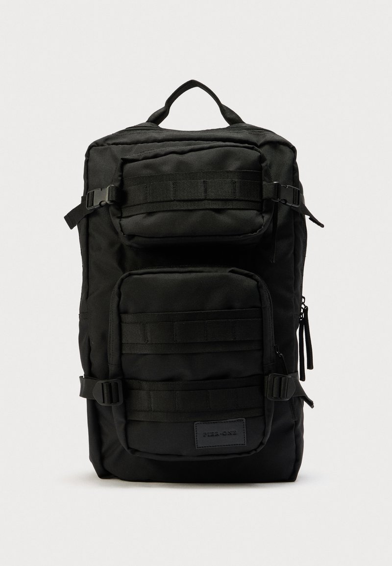 Sac à dos noir en tissu durable, doté de plusieurs compartiments, de bretelles ajustables, de fermetures éclair latérales et d'un panneau de bretelles texturé.