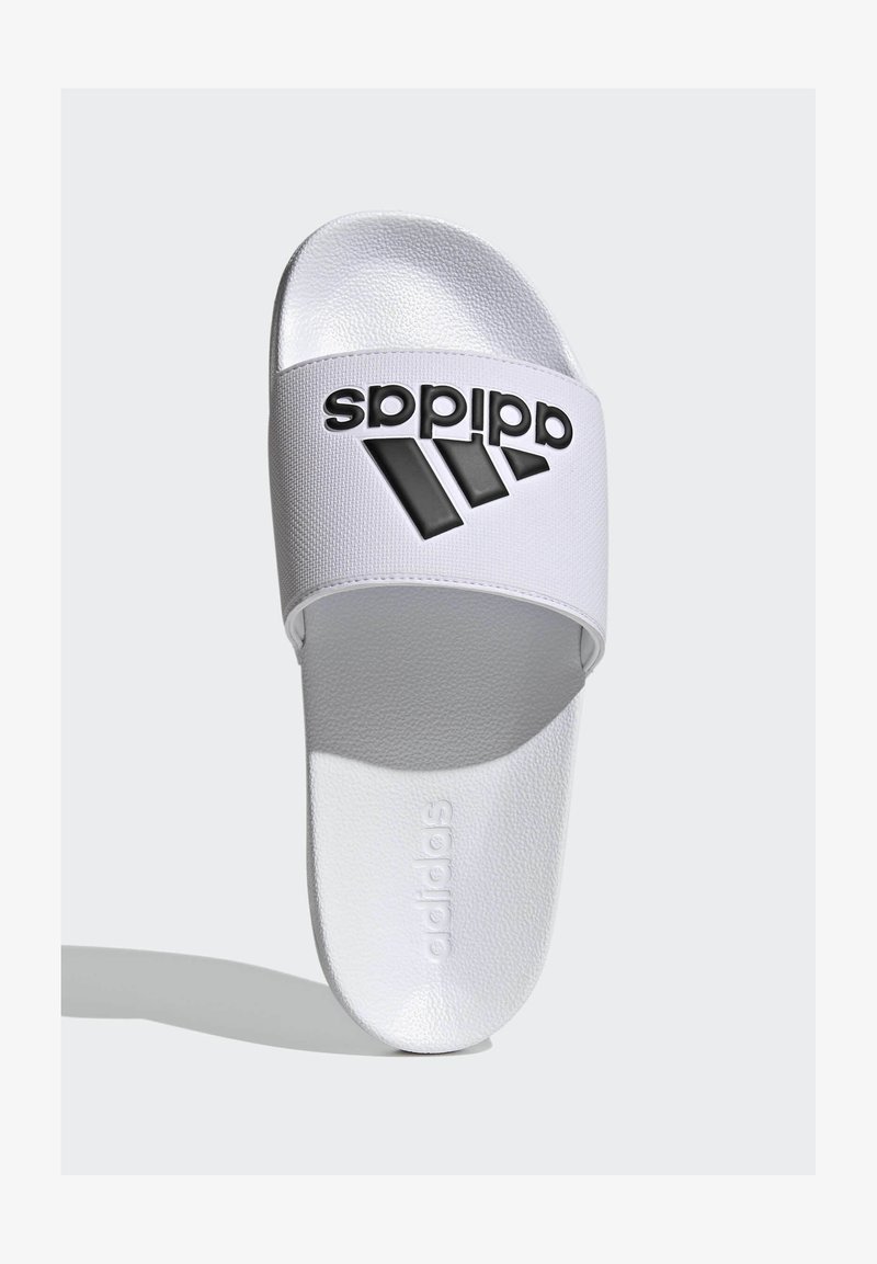 White slide sandal with a textured strap, featuring a black Adidas logo and three black diagonal stripes. Smooth white footbed with embossed branding.