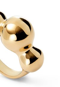 Anillo de metal dorado con dos elementos esféricos, textura suave y acabado pulido. El diseño es simple y moderno.