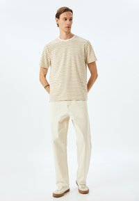 Camiseta de manga corta a rayas en beige y marrón claro, combinada con pantalones rectos de color crema y zapatillas blancas con acentos en marrón.