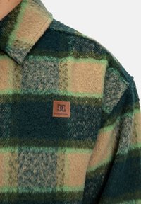 Groene, tan en blauwe geruite flanellen shirt met een zachte textuur. Bevat een kraag en een vierkant DC leren logopatch nabij de onderkant.