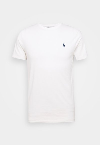 Bela bombažna majica s kratkimi rokavi in krožnim izrezom. Značilna je majhna temno modra oznaka na levem prsnem predelu. Ima kratke rokave in gladko teksturo.