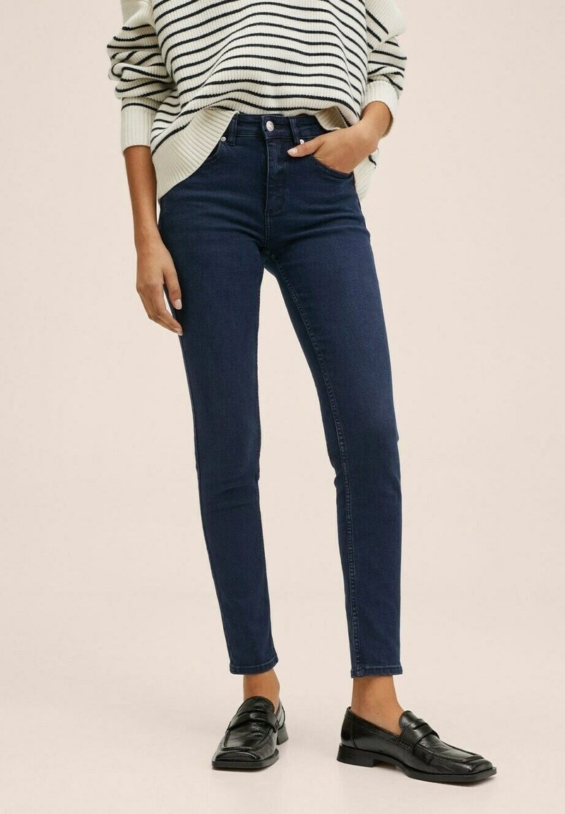 Tmavě modré skinny jeans vyrobené z denimu, s vysokým pasem a čistými liniemi. V kombinaci s pruhovaným pleteným svetrem a černými mokasíny.
