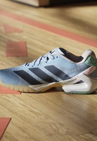 Hellblauer Sportschuh mit dunklen Streifen und dicker weißer Sohle, auf einem Holzboden drinnen platziert.