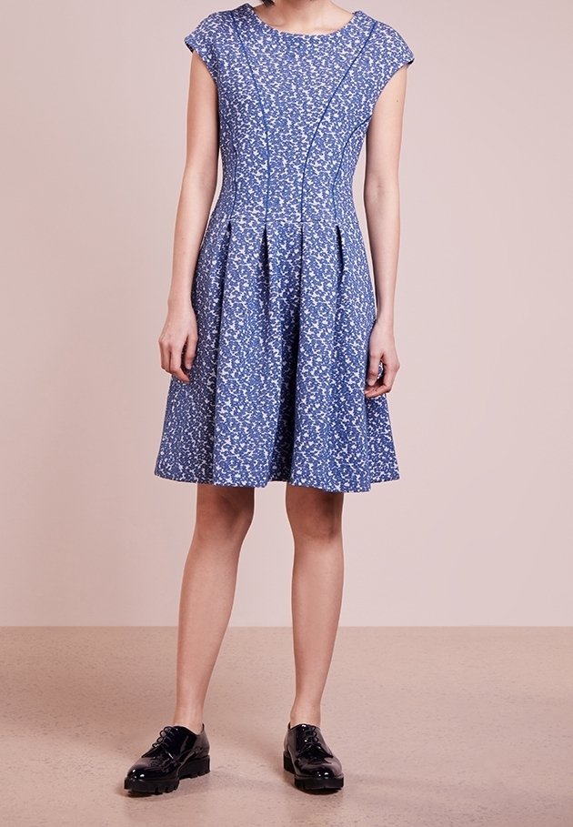 Robe bleue à fleurs avec manches courtes, corsage ajusté et jupe plissée. Fabriquée en tissu texturé, avec des détails de coutures visibles et une silhouette évasée.