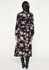 Vestido negro de manga larga con un patrón floral en tonos durazno y crema, ceñido en la cintura con un cinturón negro delgado, fluye hasta la mitad de la pantorrilla.