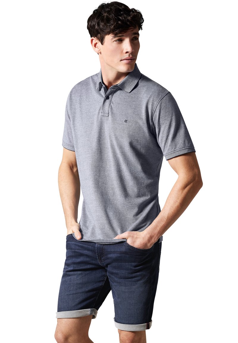 Grå polo-shirt med struktureret krave og korte ærmer, parret med mørke denimshorts med optrillede håndled. Pæne syninger synlige.