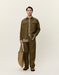 Ελαιόλαδο πράσινο μπουφάν με δύο τσέπες στο στήθος πάνω από πουκάμισο καρό, συνδυασμένο με ταιριαστά παντελόνια και καφέ τσάντα. Υφασμένο βαμβακερό ύφασμα.