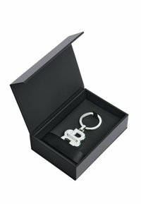 Brelok w srebrnym metalicznym wykończeniu z stylizowaną literą "B". Prezentowany w czarnym pudełku z satynową wstążką. Pudełko jest otwarte.