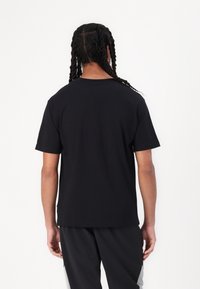 Czarna, krótka koszulka z gładkiej bawełny, z klasycznym okrągłym dekoltem i luźnym krojem, pokazana od tyłu.