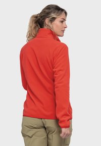 Red fleece pullover with a high collar, featuring long sleeves and a soft texture, paired with khaki pants.