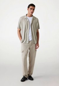 Kortærmet, lysegrå skjorte med knapper og tekstureret finish, kombineret med beige cargobukser og sorte slip-on sko.