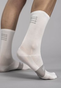 White athletic socks with a mesh texture and grey logo/accents. Features a reinforced toe and heel, and subtle striped pattern at the cuff.
