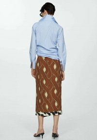 Blauwe gestreepte blouse, losse pasvorm, met knoopsluiting en kraag. Bruine geprinte rok met gele accenten en zwarte zoom. Open teen zwarte hakken.