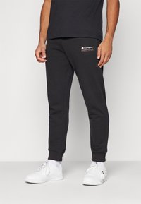 Melni sporta bikses, kas izgatavotas no kokvilnas un poliesteru maisījuma, ar ribotu jostu un piedurknēm. Champion logotips sarkanā krāsā kreisajā augšstilbā.