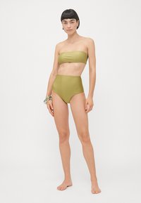 Conjunto de bikini verde oliva com top sem alças e calções de cintura alta. Textura suave e design minimalista sem hardware visível.