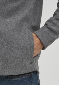 Grå fleece-sweatshirt med teksturert finish, med sidelommer, en liten logo ved kanten og lange ermer.