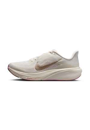 Lichtbeige Nike hardloopschoen met een gouden Swoosh, ademend mesh-bovenwerk en dikke gevoerde zool met rode accenten.