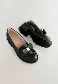 Černé lakované kožené loafers mají detail mašle se zlatým akcentem, strukturovaný svršek s vzorovaným prošíváním a masivní gumové podrážky.