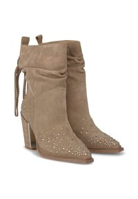 Botas de tobillo de ante en color beige con un diseño holgado, adornadas con tachuelas metálicas, punta afilada y un tacón grueso. Presentan lengüetas de tirón y lazos laterales.
