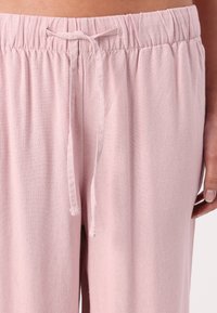 Pantalons rose à cordon de serrage, fabriqués dans un tissu léger avec une taille froncée et une texture douce. Présentent un design simple et une coupe décontractée.