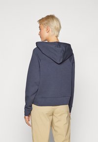 Hanorac bleumarin cu glugă ajustabilă, manșete ribbate și un design scurt. Fabricat dintr-un material moale din amestec de bumbac. Simplu, fără modele.