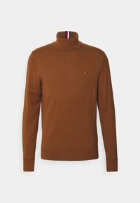 Brun rullekrave-trøje lavet af blødt stof. Har en tætsiddende pasform, ribstrikkede manchetter og en lille logo på brystet med røde og hvide detaljer.