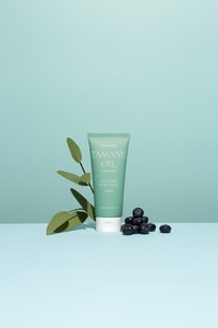 Grüne Kunststofftube mit der Beschriftung "Tamanu Oil Soothing Scalp Pack" und weißen Akzenten, platziert neben dunklen Heidelbeeren und grünen Blättern auf einem hellblauen Hintergrund.
