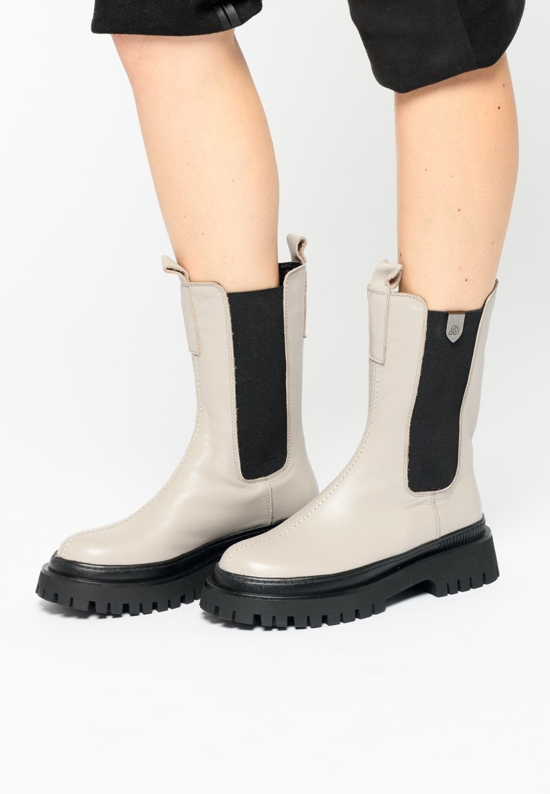 Botines beige de cuero con paneles laterales elásticos negros y suelas de goma ranuradas, con lengüetas para facilitar su colocación.