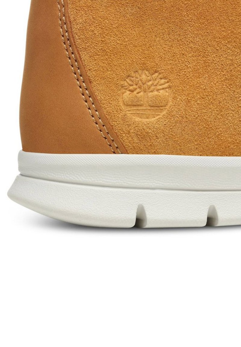 Sneaker in camoscio e pelle color sabbia con suola in gomma bianca, dettagli cuciti e logo ad impressione. Texture morbida e forma arrotondata.