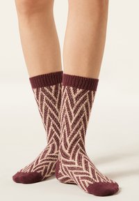 Chaussettes en tricot bordeaux et crème avec un motif en zigzag. Bord-côte côtelé et orteils unis bordeaux. Longueur mi-mollet, texture douce.