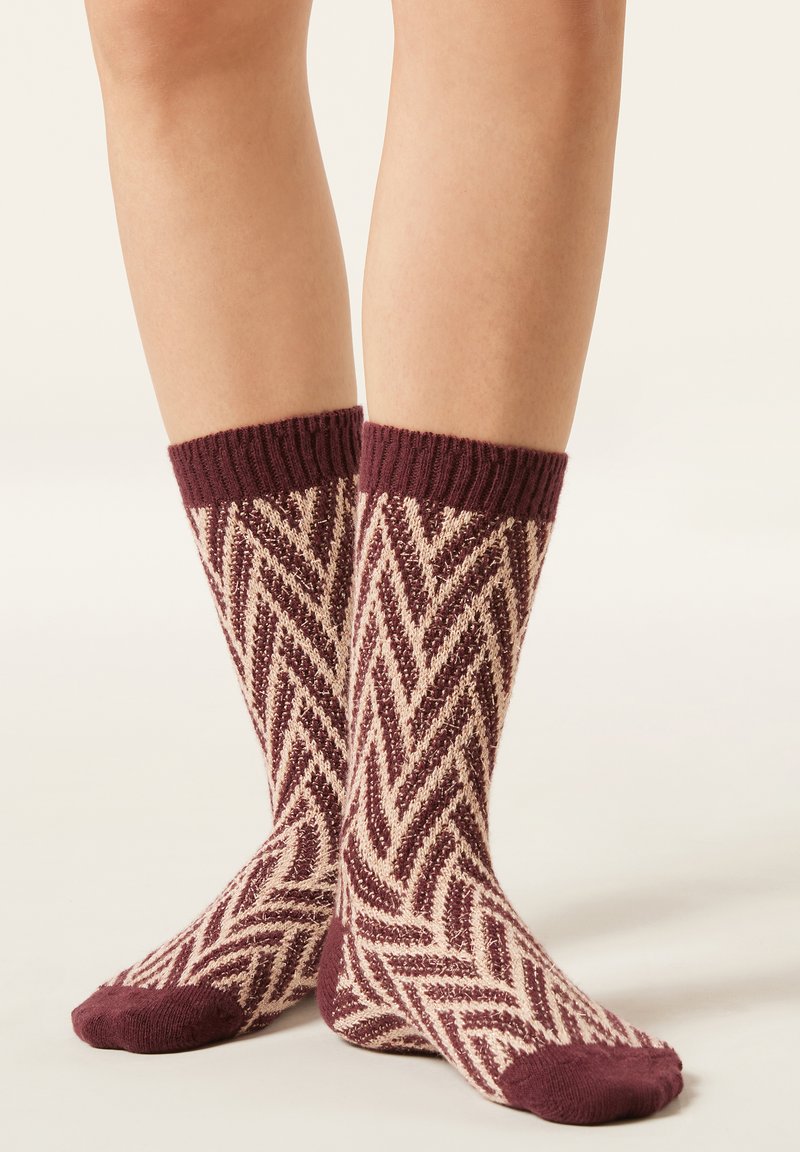 Chaussettes en tricot bordeaux et crème avec un motif en zigzag. Bord-côte côtelé et orteils unis bordeaux. Longueur mi-mollet, texture douce.