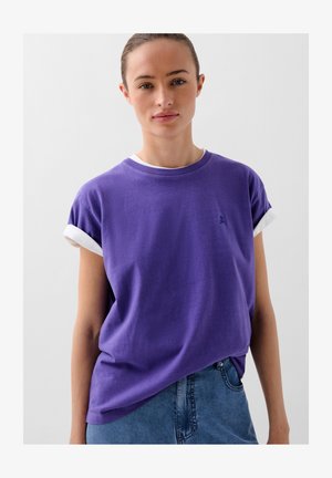 Lila Kurzarm-T-Shirt mit einem weißen umgeschlagenen Saum, versehen mit einem kleinen gestickten Logo auf der Brust, lockere Passform und aus weichem Baumwollstoff.