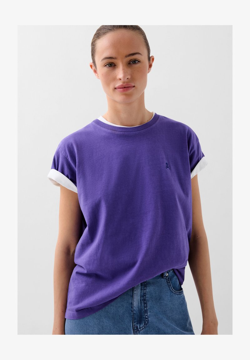 Lilla kortærmet T-shirt med en hvid rullet kant, der har et lille broderet logo på brystet, afslappet pasform og blødt bomuldsstof.